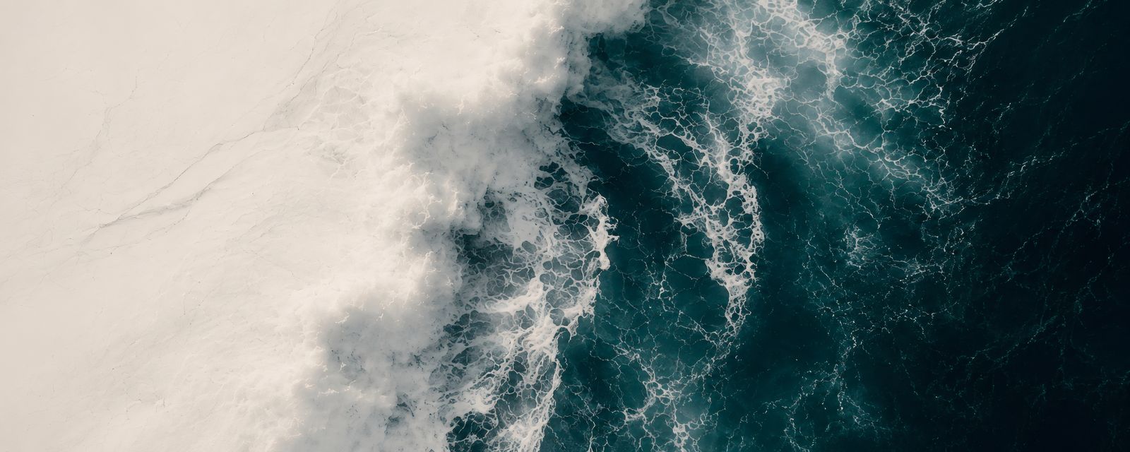 Brandung aus der Luft: weißer Schaum trifft auf tiefgrünes Wasser